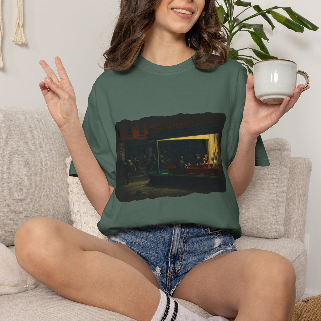 Woman sitting on a cream sofa wearing blue spruce colour  tshirt with graphic image inspired by Edward Hopper's Nighthawks 