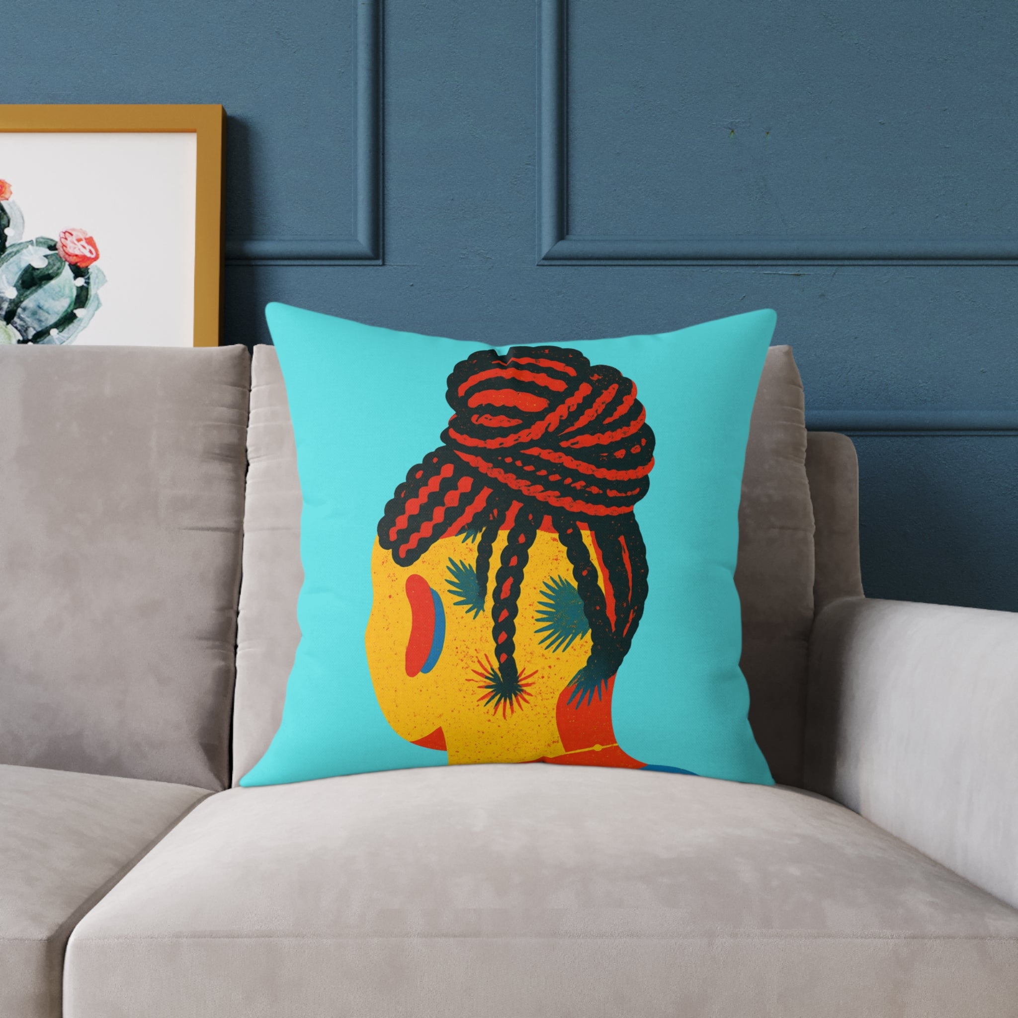 Colorful pillow with a design of braided hair on a gray sofa against a blue wall.