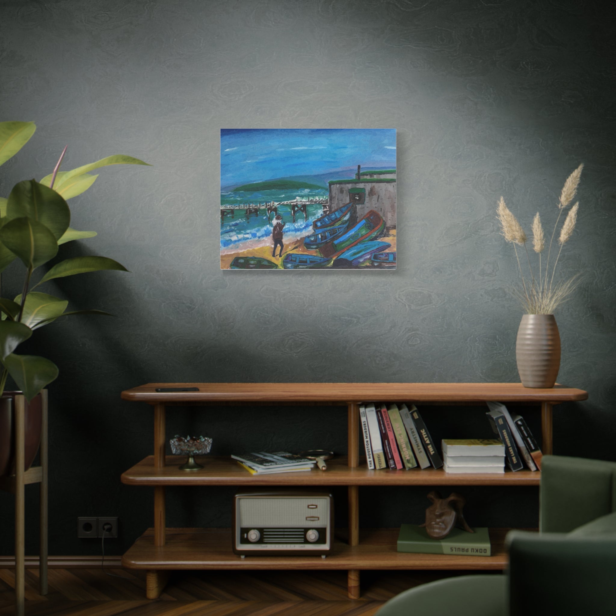 Living room with a painting of a coastal scene on the wall, a shelf with books and a radio, and a plant.