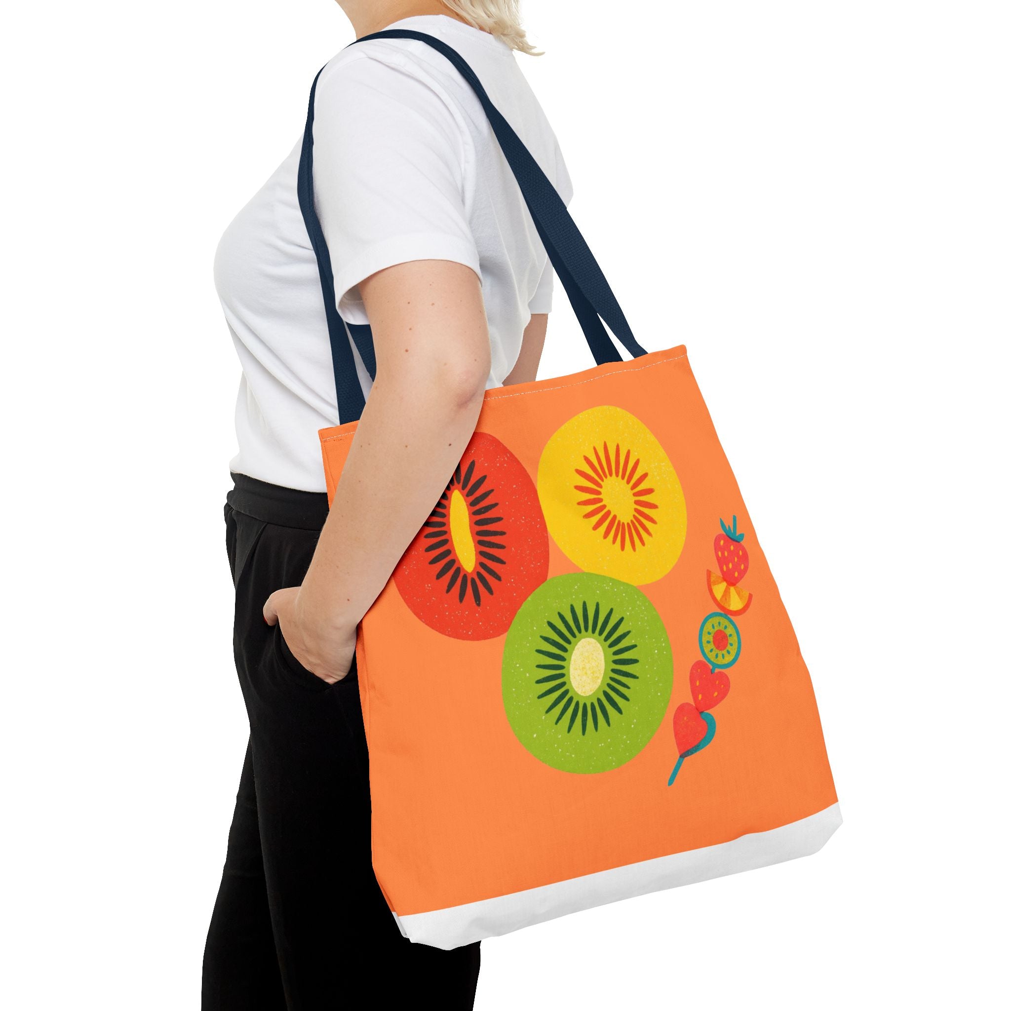 Person holding an orange tote bag with fruit designs on a white background