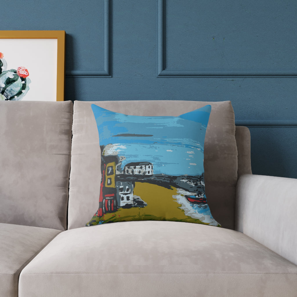 Decorative pillow with a colorful coastal scene on a beige sofa against a blue wall.
