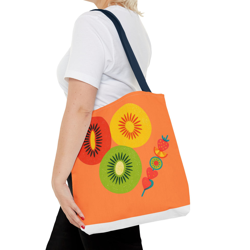 Person holding an orange tote bag with colorful fruit designs on a white background