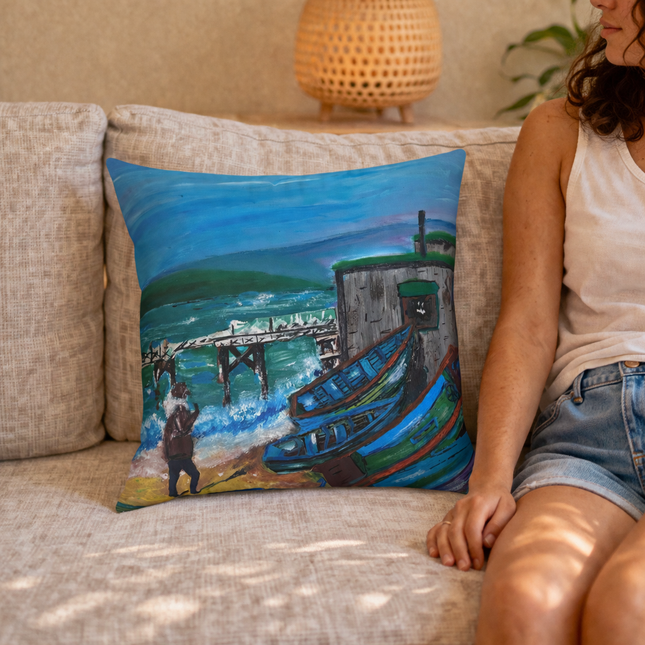 Person sitting on a couch with a decorative pillow featuring a painting of a boat and pier.